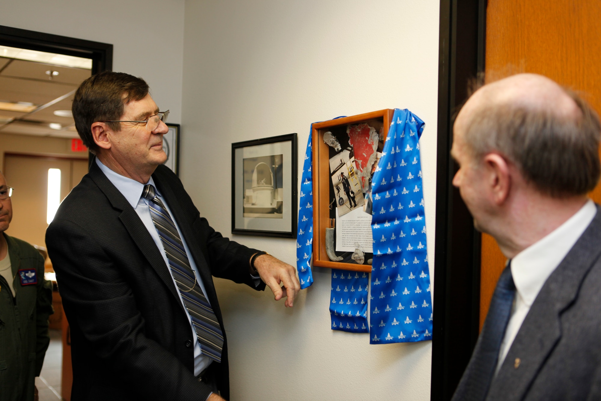 Ted Wierzbanowski from Class 80B unveils a shadow box outside the Carmen Lucci Control Room March 17 during the dedication ceremony. Wierzbanowski spent a significant amount of time with Lucci while they were both students at the United States Air Force Test Pilot School. Lucci was killed during a test mission March 3, 1981. She is the first female flight test engineer to lose her life either as a student or graduate of the four formal test pilot schools. (Air Force Photo by Jet Fabara)