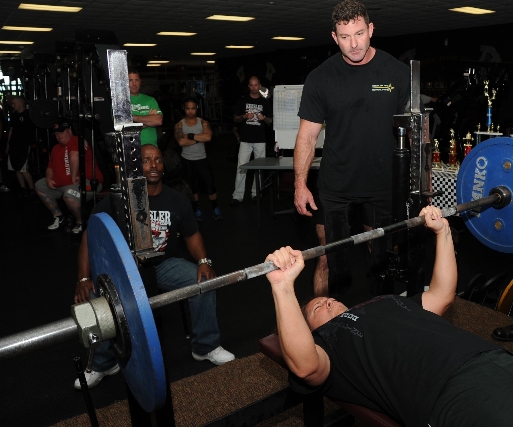 Staff Sgt. Amy Lolo, 336th Training Squadron,  takes her turn during the bench press portion of the muscle mania competition, while Al Watkins, 81st Infrastructure Division, serves as the judge and Robert Reville spots her March 24, 2012, at the triangle fitness center, Keesler Air Force Base, Miss.  Lolo placed third overall in the women’s division.  (U.S. Air Force photo by Kemberly Groue)