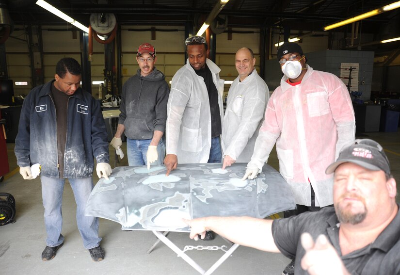 Team Andrews members point to the repairs they made to a dented car hood during an auto body class at the Andrews Auto Hobby Center on March 25.  Harvey McKenzie, an auto body technician form Maaco of Waldorf, lower right, showed the attendees how to prepare, repair and refinish the damaged hood themselves using tools and materials available at the auto hobby center.  (U.S. Air Force photo/Senior Airman Torey Griffith)(released)