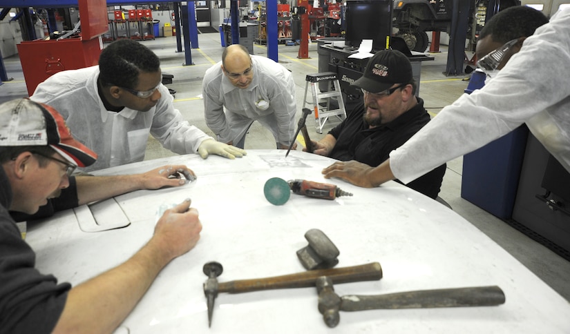 Harvey McKenzie, a professional auto body technician from Maaco of Waldorf, shows Team Andrews members how to repair a dent in a car hood using special hammers and metal shaping tools called dollies.  This method minimizes the use of body filler to make the damaged surface straight again.  McKenzie is a third generation body man, and uses many "old school" methods to achive the flawless results required when working on restoration and custom jobs. (U.S. Air Force photo/Senior Airman Torey Griffith)