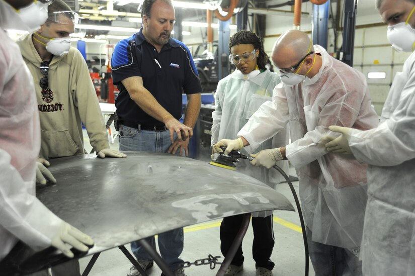Paul Faucheux, owner of Maaco of Waldorf, instructs Team Andrews members as they sand a car hood with a dual-action sander during a body shop class at the Andrews Auto Hobby Center on March 25.  Faucheux sponsored the class, which was an introduction to the fundamentals of basic body repair and refinishing. (U.S. Air Force photo/Senior Airman Torey Griffith)(released)