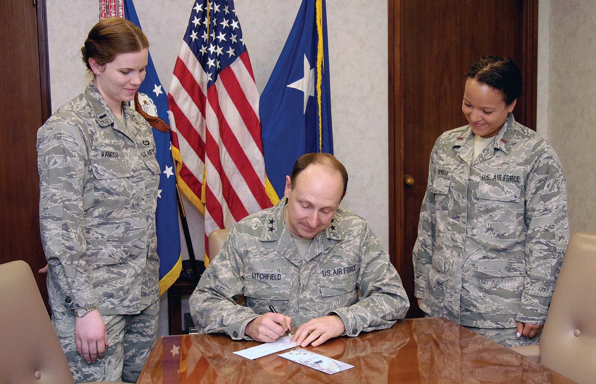 Oklahoma City Air Logistics Center Commander Maj. Gen. Bruce Litchfield signs a pledge form for Tinker’s Air Force Assistance Fund drive recently.  Assistant installation project officer 1st Lt. Elizabeth Ramoso, left, and OC-ALC key worker 2nd Lt. Kim Madorran met with the commander about Tinker’s annual drive that runs through April 13. (Air Force photo by Margo Wright)