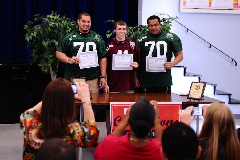 BITBURG ANNEX, Germany – Colton Engelmeier, left, Matthew Flood, center, and Darian Billups pose for photos to commemorate their selection to the Military.com All-Department of Defense Team at Bitburg High School here March 27. The team is made up of 24 football players who are children of service members stationed throughout the world. Military.com is a military and veteran membership organization that connects service members, military families and veterans to all the benefits of service. The BHS football team members received a certificate and a team jersey, and will attend an upcoming invitation-only 2012 Football University Camp, taught by NFL coaches and players. The team members will find out at a later date which one of the 45 camps they will be invited to attend. (U.S. Air Force photo by Airman 1st Class Matthew B. Fredericks/Released)