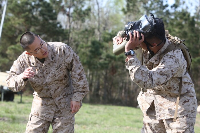 Cpl. Jason J.  Cheng (left), a chemical, biological, radiological and nuclear warfare specialist with Combat Logistics Regiment 27, 2nd Marine Logistics Group, shows a Marine from Landing Support Company, CLR-27, 2nd MLG how to drink out of a canteen with a gas mask on during a CBRN readiness exercise aboard Camp Lejeune, N.C., March 28, 2012. The training also included how to react to an attack and how to properly wear Mission-Oriented Protective Posture suits.