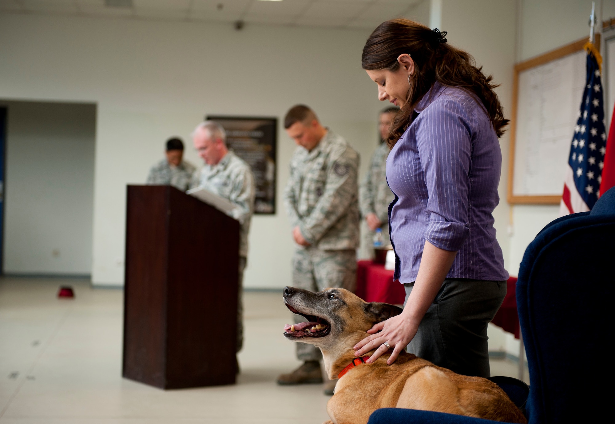 Stacey Ball, owner of former military working dog, Max, pets the dog to keep him calm during the invocation at his retirement ceremony March 23, 2012 in the 39th SFS guardmount room at Incirlik Air Base, Turkey. Max now lives with Mrs. Ball and her husband, Staff Sgt. Joshua Ball, 39th Maintenance Squadron. (U.S. Air Force photo by Senior Airman William A. O'Brien/Released)