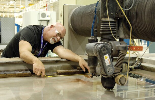Carl Massey measures cuts made on a sheet of metal by a water jet that uses high-pressure water and garnet grit to carve blank metal into a needed part.  Here he cuts out a test box for an F15 heat exchanger. (Air Force photos by Margo Wright)
