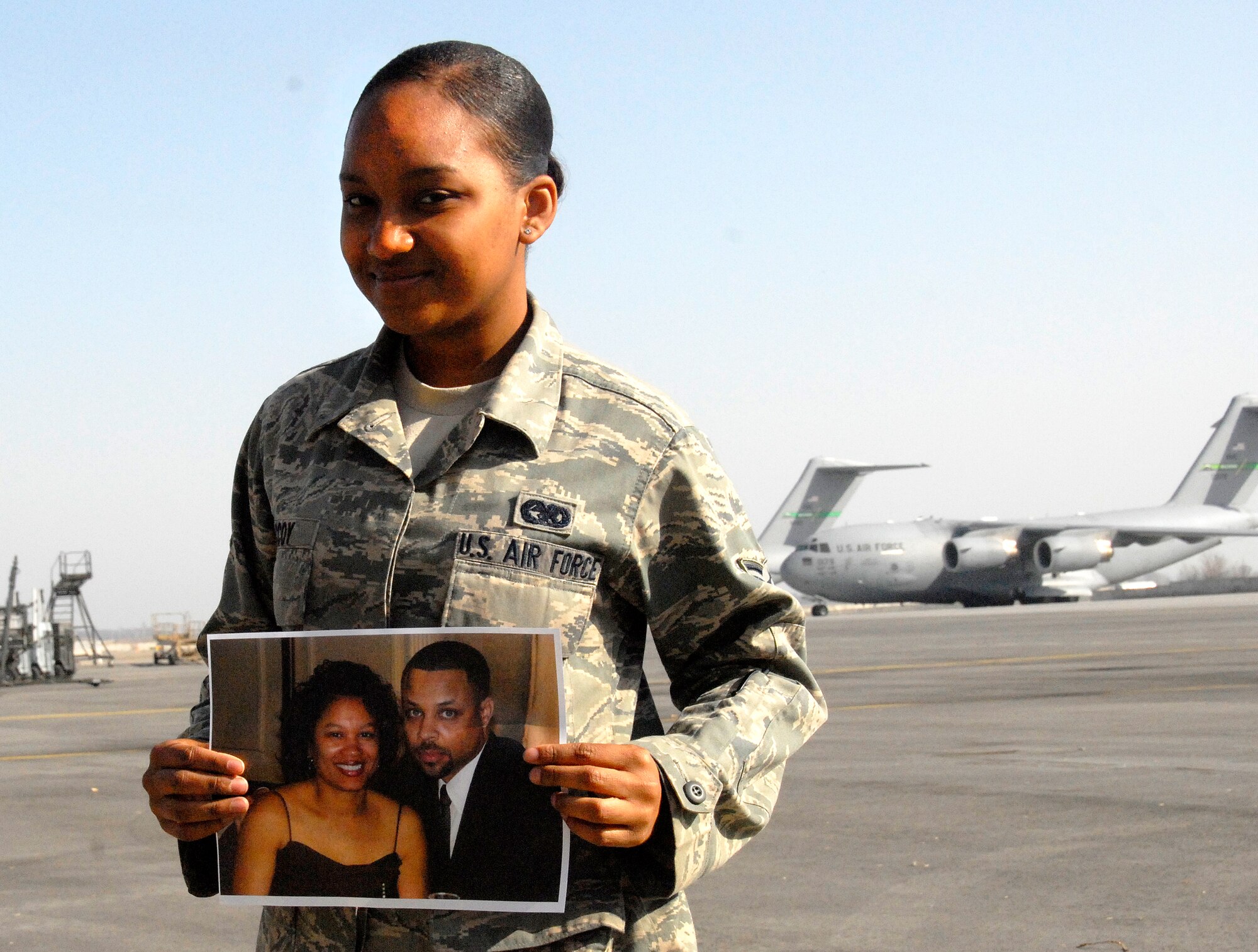 Airman 1st Class Marita McCoy, 376th Expeditionary Logistics Readiness Squadron traffic management office, holds a picture of her stepmother and father on the flight line at the Transit Center at Manas March 31, 2012. McCoy?s stepmother works with the Defense Biometrics Identification Systems, which is a part of the 376th Expeditionary Force Support Squadron here. Her father is a 376th Expeditionary Operations Group air traffic controller instructor. This is McCoy?s first deployment. She is deployed here from Whiteman Air Force Base, Mo. (U.S. Air Force photo/Senior Airman Lynsie Nichols)