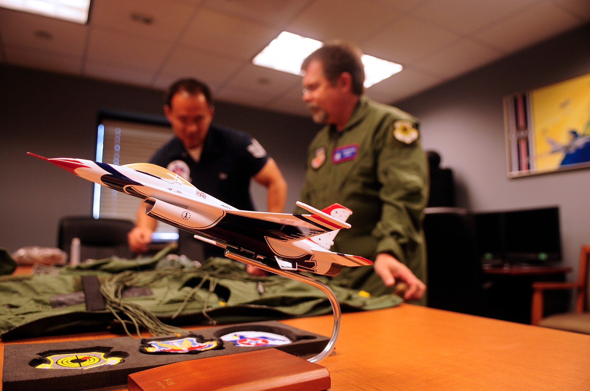 A miniature replica of a Thuderbird aircraft is in the foreground of U.S. Air Force Tech. Sgt. Sang Lee, Thunderbirds' aircrew flight equipment member, as he trains Derek Burress, the host for the “Good Morning Sumter” broadcast, how to properly use his equipment prior to his flight equipment at Shaw Air Force Base, S.C., May 2, 2012. The Thunderbirds are at Shaw for the Shaw Air Expo May 5 and 6. The Shaw Air Expo will have aircraft performances as well as entertainment from the Heritage of America Band, the Blue Aces. (U.S. Air Force photo by Airman 1st Class Hunter Brady/Released) 