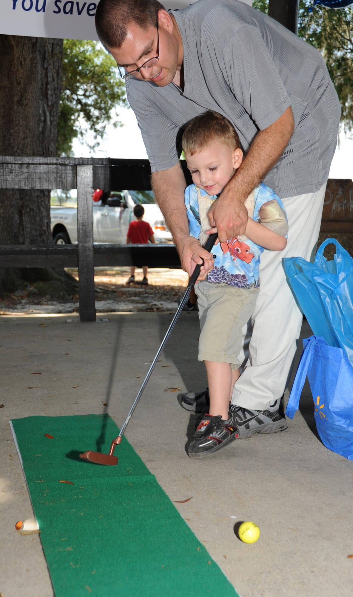 Senior Airman Shane Van Dusen, 345th Airlift Squadron, helps his son, Gabriel, 3, with playing putt-putt golf during Child Pride Day April 28, 2012, at Marina Park, Keesler Air Force Base, Miss.  Child Pride Day is an annual event held in conjunction with the month of the military child.  Booths, jumpers, activities, entertainment and food were set up throughout the park.  (U.S. Air Force photo by Kemberly Groue)