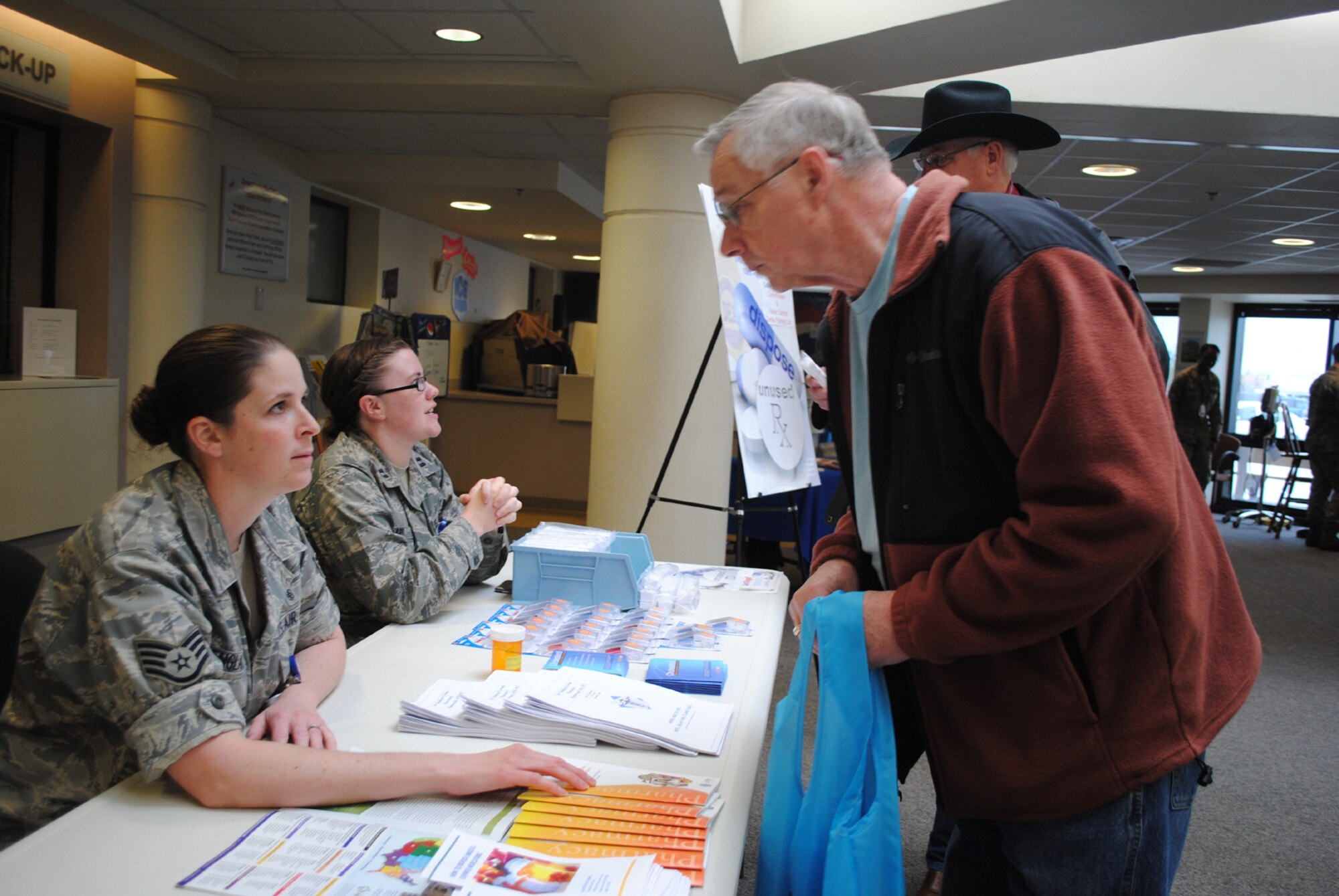 Staff Sgt. Traci England, 341st Medical Operations Squadron NCO in charge of out-patient pharmacy, left, gives Bill Nazelrod a variety of brochures at the pharmacy booth set up at the clinic as Capt. Julie Ward, 341st Medical Support Squadron pharmacist, discusses recycling unused drugs with David Polmanteer. (U.S. Air Force photo/John Turner)