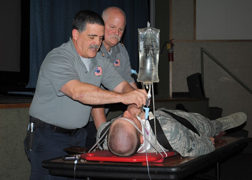Airman 1st Class Cody Carvey, 341st Missile Security Forces Squadron member, lays on a backboard as Ronny Garcia simulates a tracheotomy; Greg McCarty stands by. Garcia and McCarty are firefighter paramedics from Florida who held Street Smart presentations on Malmstrom April 30. (U.S. Air Force photo/Airman 1st Class Cortney Paxton)