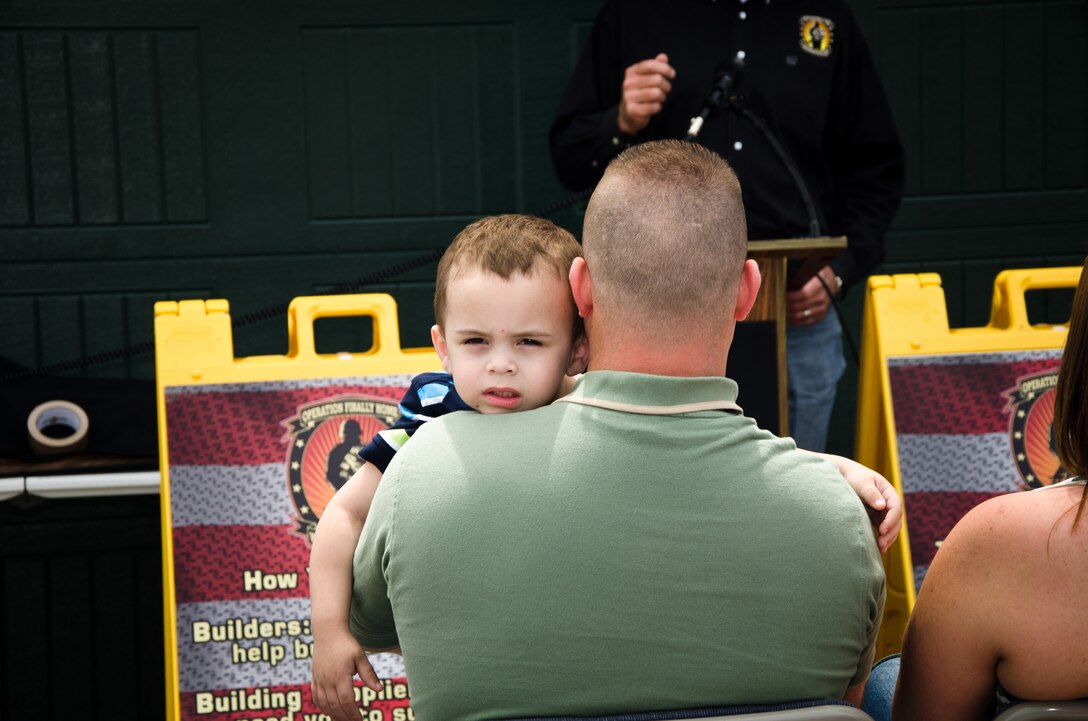 Retired Marine Staff Sergeant Vincent Gizzarelli holds his adopted son during the dedication ceremony of his family's brand new house, Jacksonville, N.C., Apr. 28. The house was built using supplies and donations from local businesses and various veterans' groups. Gizzarelli was medically retired from the Marine Corps after suffering traumatic brain injury and shrapnel wounds from multiple IED blasts that he sustained on his second tour to Iraq. 