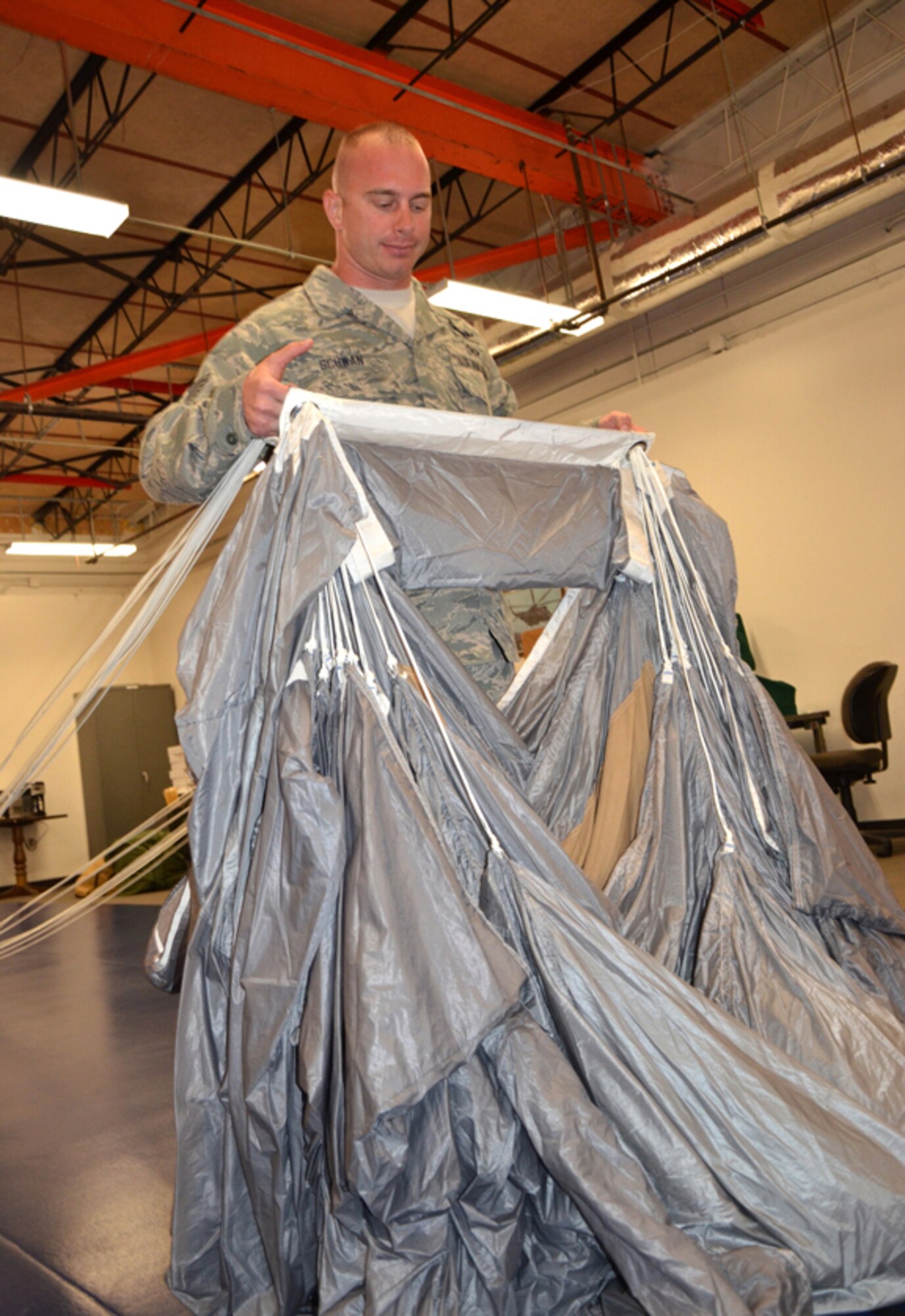 Tech Sgt. Christopher Schwan, 920th Rescue Wing, Patrick Air Force Base, Fla., Aircrew Flight Equipment Specialist reservist, holds up a parachute used by combat search and rescue operators here. Schwan was honored as the Recruit Fire Fighter of the Year for Brevard County. He was chosen out of 70 recruits for 2012. As a fire fighter, Schwan uses the same inspiration he uses here, saving lives. "I love both of my jobs, they both give me the opportunity to save a life," said Schwan. (U.S. Air Force photo/2nd Lt. Leslie Forshaw)