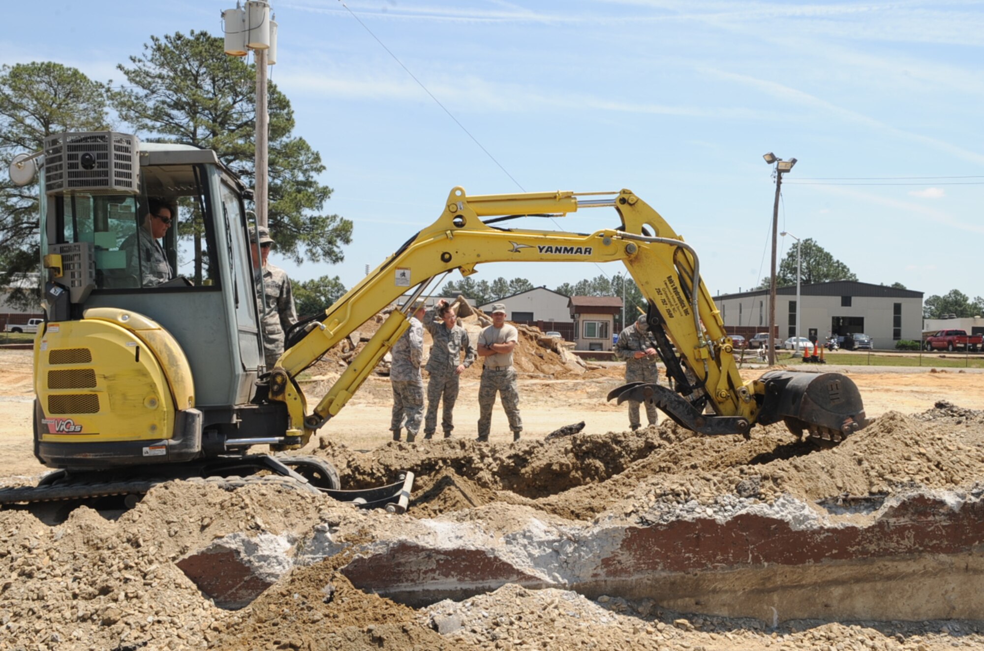 U.S. Air Force Airmen watch Col. Anne Winkler attempt to lift concrete debris using a miniature excavator during a construction project in tent city on Seymour Johnson Air Force Base, N.C., May 3, 2012. The old concrete is being broken up and moved in order to make space for new slabs. Instead of having one large concrete pad, there will be one slab of concrete per tent. Winkler, 4th Mission Support Group commander, is a native of Kansas City, Mo. (U.S. Air Force photo/Airman 1st Class Aubrey Robinson/Released)