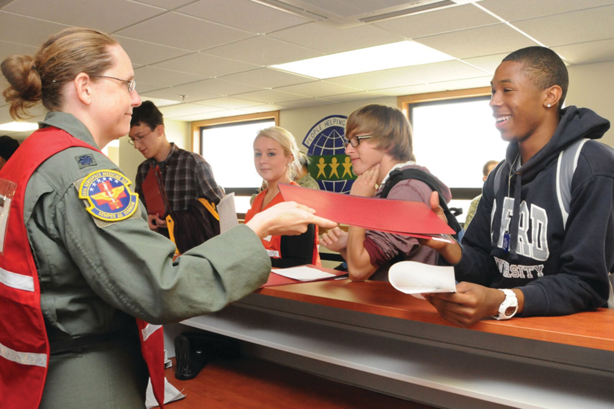 Lt. Col. Christine Tholen, 65th Medical Group chief of aerospace medicine, gives DeMarcus Hodge, son of Lt. Col. Gwendolyn Johnson, 65th Medical Operations Squadron commander, his "mock" medical records during a base exercise where middle and high school students prepared to deploy April 26.  (U.S. Air Force photo/Kennedy Lewis)
