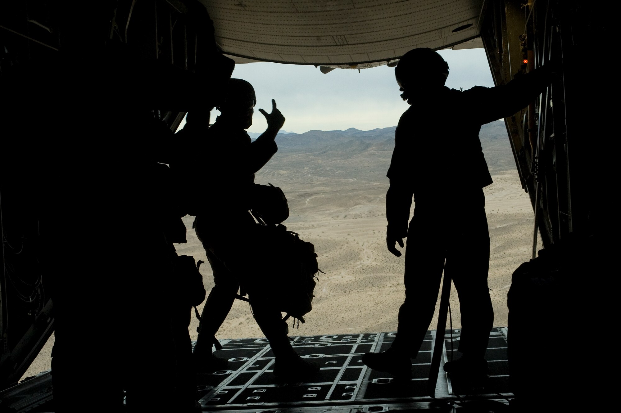 U.S. Air Force Tech. Sergeant Romag, 820th RED HORSE Squadron airborne flight jump master, signals to Airmen during a sling load training jump from a Wyoming Air National Guard C-130 Hercules April 24, 2012, at Nellis Air Force Base, Nev. The jumpmaster's responsibilities consist of getting paratroopers trained properly, getting them to the aircraft, and getting them safely delivered to the ground. (U.S. Air Force photo by Staff Sgt. Christopher Hubenthal)
