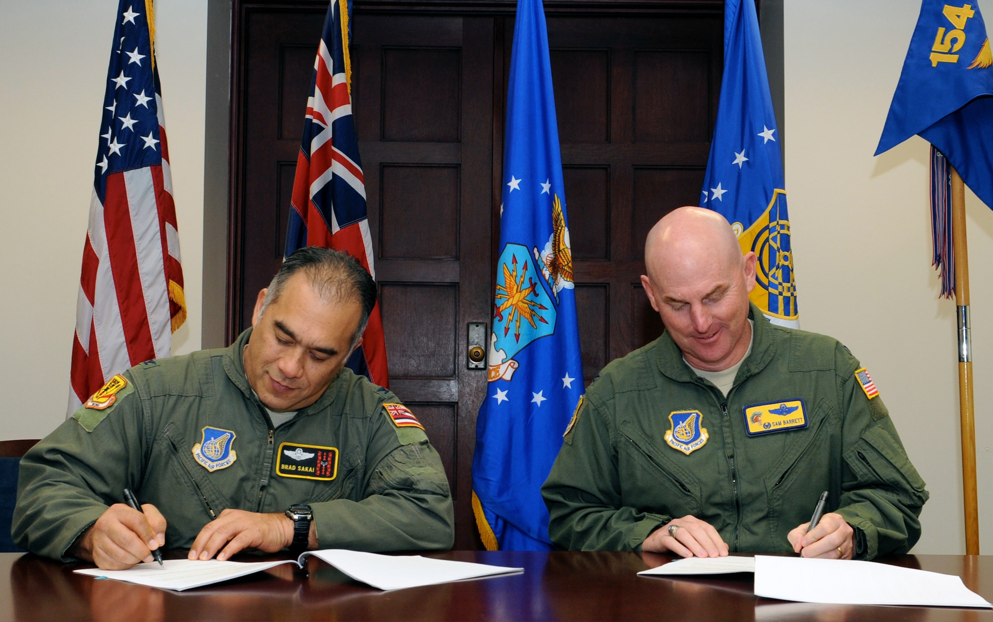 Brig. Gen. (Sel.) Braden Sakai, 154th Wing Commander, and Col. Sam Barrett, 15th Wing Commander, sign copies of the Memorandum of Understanding between the 15th and the 154th Wings, March 16, defining Total Force Integration at Joint Base Pearl Harbor-Hickam. The Wings work in partnership to employ Total Force combat and peacetime support to operations across Hawaii and throughout the Pacific Theater. Under this Total Force construct, the 15th and 154th Wings retain their separate administrative organizational structures and chains of command while functionally integrating to achieve unity of effort to accomplish Wing missions. (U.S. Air Force Photo by Senior Master Sgt. Kristen Stanley)