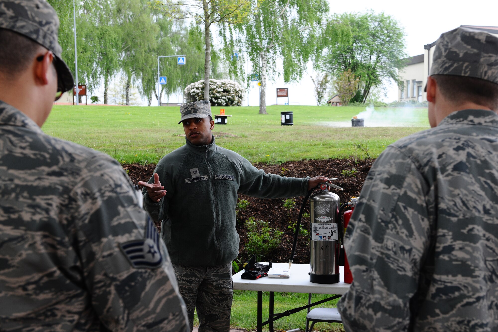 SPANGDAHLEM AIR BASE, Germany – Tech. Sgt. Daniel Robinson, center, 52nd Civil Engineer Squadron firefighter, explains the uses of the three different types of fire extinguishers to 52nd Fighter Wing Airmen during individual core competency skills training at the outdoor basketball court here May 7. The training evaluated Airmen on their combat readiness skills such as M-4 assault rifle weapons knowledge; self-aid buddy care; and chemical, biological, radiological, nuclear, and high-yield explosive preparedness. The training ensures the 52nd Fighter Wing is able to provide combat power to the current fight. (U.S. Air Force photo by Airman 1st Class Dillon Davis/Released)