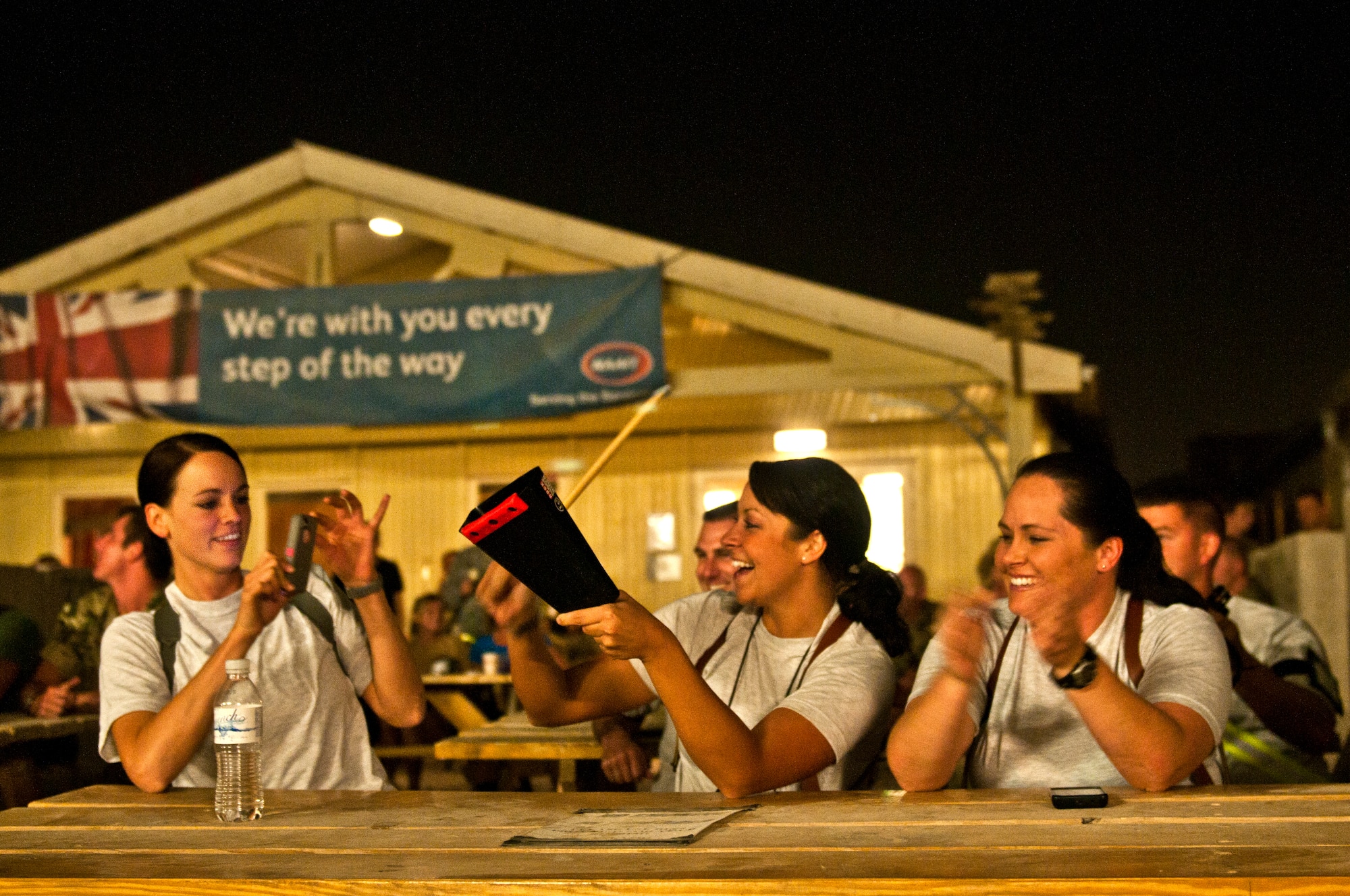 From left, Tech. Sgt. Caycee Cook records Airman 1st Class Lauren Narduzzi playing the cowbell as Master Sgt. Alison Schier cheers her on May 2, 2012 at Kandahar Airfield, Afghanistan. During Nightwing’s concerts, they often perform Saturday Night Live’s skit -- 'Cowbell', handing out several cowbells to audience members. (U.S. Air Force photo by Staff Sgt. David Salanitri/Released)