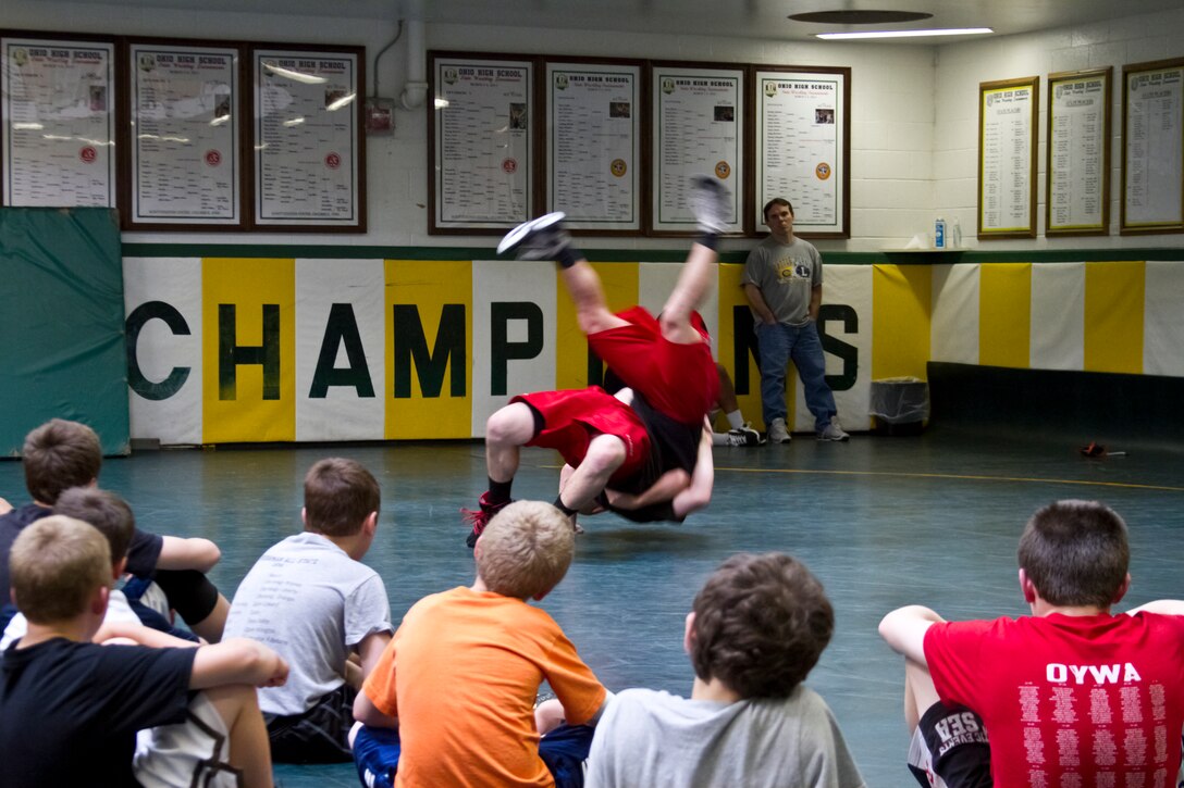 Young wrestlers watch as Cpl. Donald Simmons throws fellow All Marine Wrestling Team member 1st Lt. Joel Ahern to the mat during a Marine led wrestling clinic at St. Edward High School, May 9. Greco-Roman wrestling, the style being taught by the Marine wrestlers, forbids the use of legs or going for opponents’ legs so wrestlers rely on throws to bring each other to the ground.