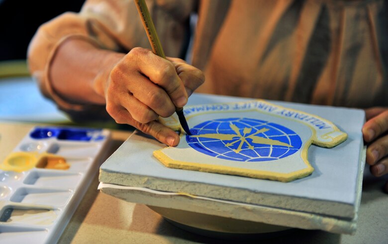 Artist Claudia Gullet paints a shield in her basement studio April 27, 2012. The shield one of the 300 ceramic tiles that comprises the mural to be placed in the new Student Union on Scott Air Force Base, Ill. in June 2012. (U.S. Air Force photo/ Staff Sgt. Stephenie Wade)