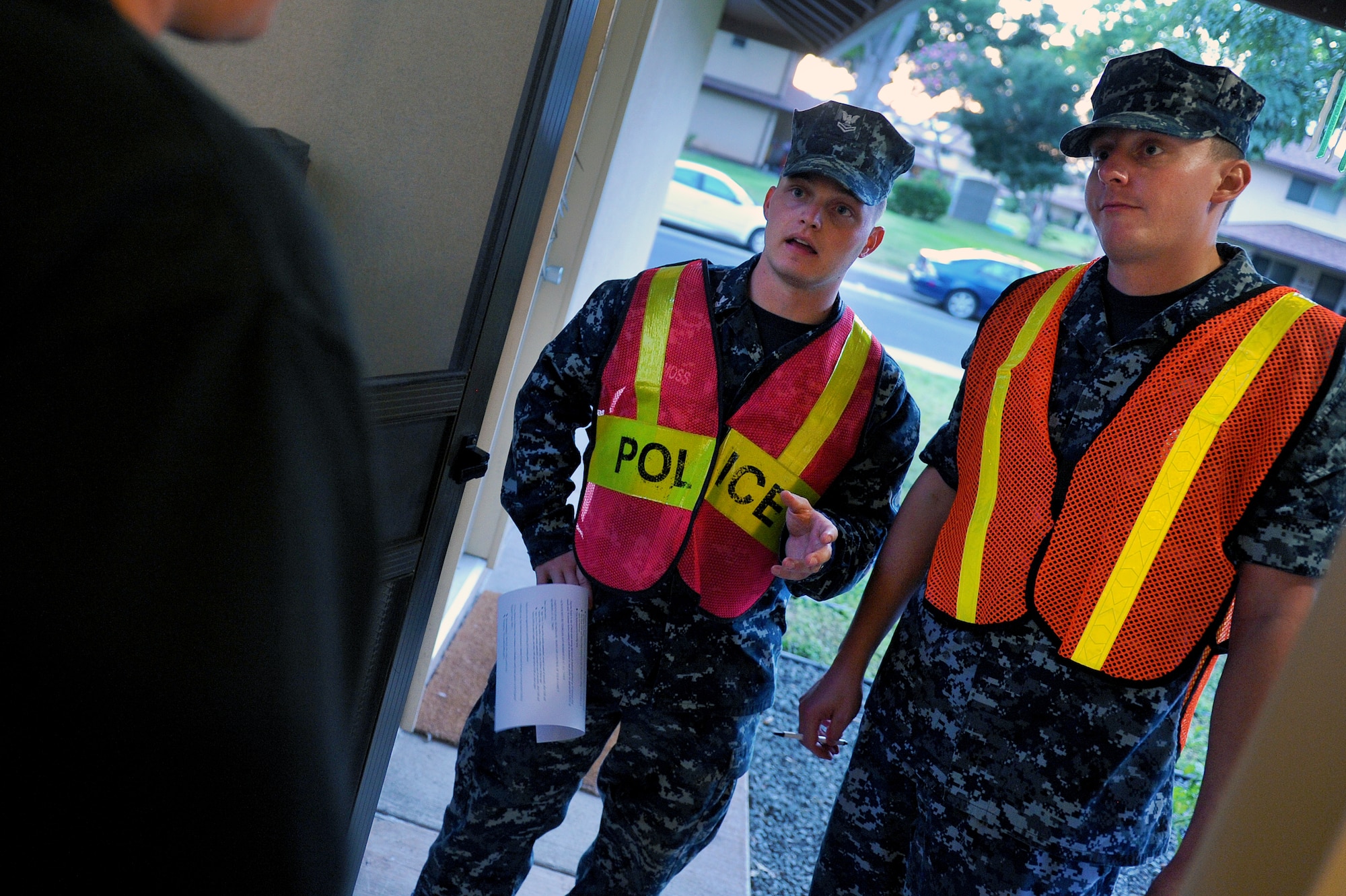 Petty Officer 2nd Class Tim Moss and Seaman Scott Meyer, Pearl Harbor harbor patrolmen, speak to Master Sgt. Tony Karpenko, 647th Logistics Readiness Squadron Fuels flight, on Hickam Field as they go door-to-door during Operation ENLIGHTEN II, May 9, where Airmen and Sailors went to more than 2,000 homes to hand out information about safety and security. In response to a rash of crimes ranging from petty theft to grand larceny, Joint Base Pearl Harbor-Hickam officials engaged residents in the anti-crime campaign. More than 120 volunteers went door-to-door during the blitz event. (U.S. Air Force photo/Staff Sgt. Mike Meares)