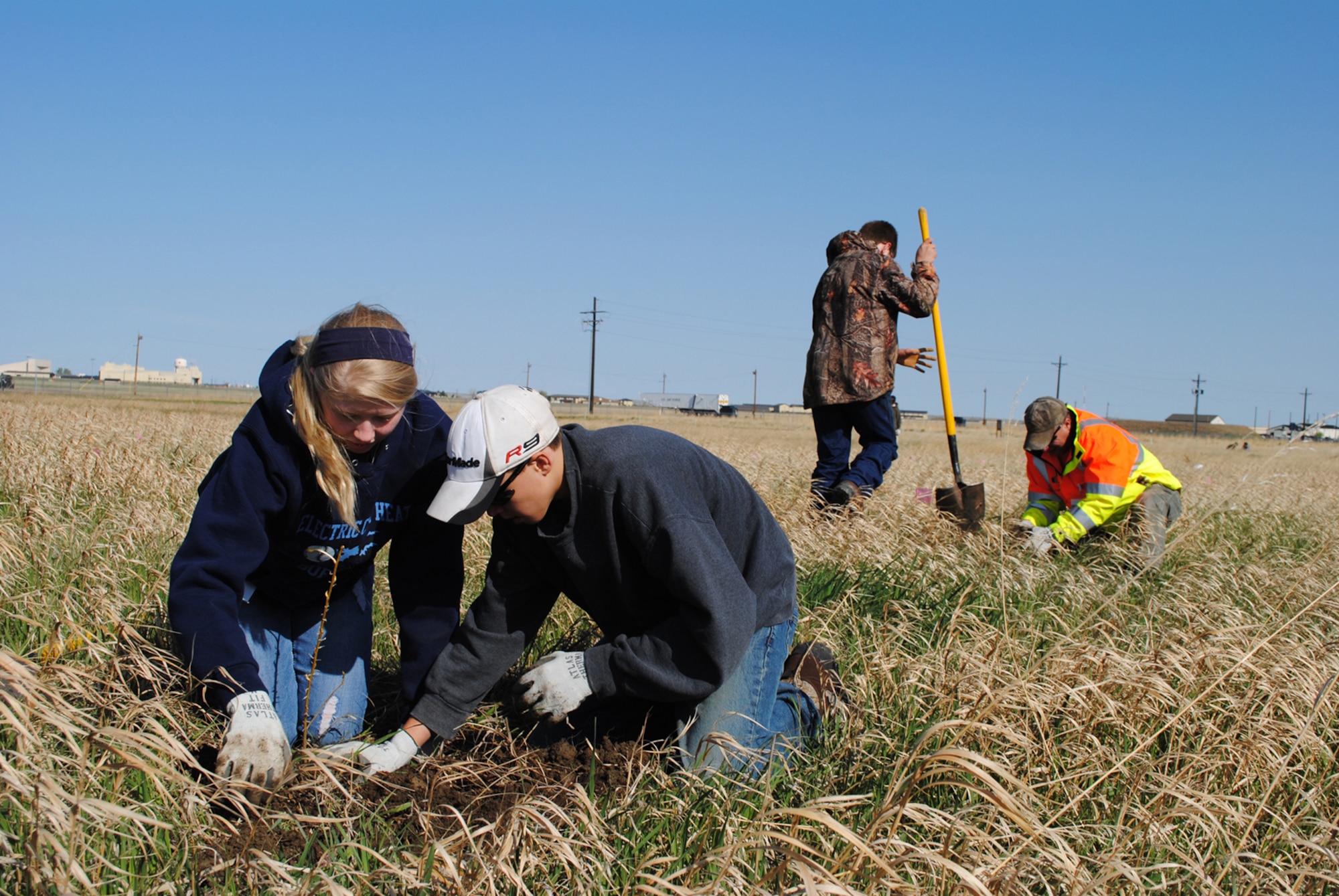 Great Falls High School freshmen Measha Lindstrand and Dalton Meeks pat down soil to ensure all air pockets are removed as Madison Brady, GFHS freshman, helps Jonathan Meeks, adult volunteer, dig a hole in the background. (U.S. Air Force photo/Airman 1st Class Katrina Heikkinen)