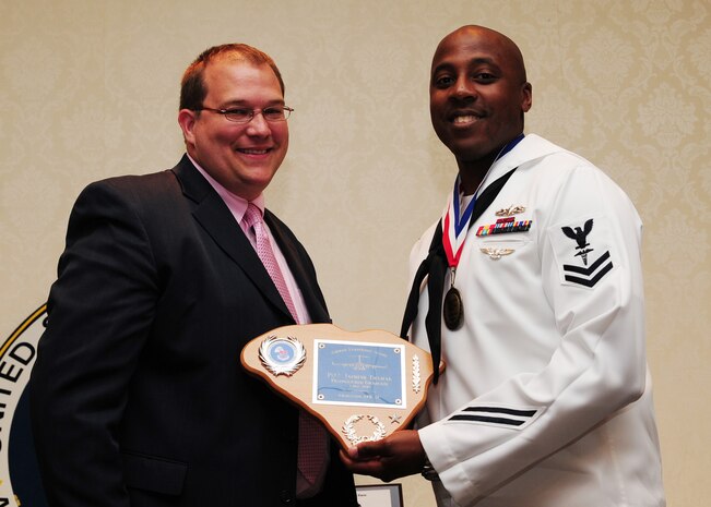Dave Thompson, First Command Financial Services, presents a Distinguished Graduate Award to Petty Officer 2nd Class Japheth Tillman, Naval Health Clinic Charleston advanced x-ray technician, during the Airman Leadership School Class graduation May 4 at Joint Base Charleston - Air Base. The Distinguished Graduate Award is presented to the top 10 percent of students with the highest overall average in all graded areas. (U.S. Air Force photo/Staff Sgt. Katie Gieratz)