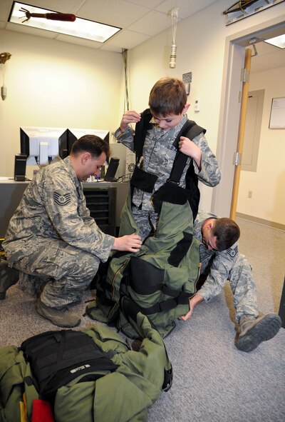 Tech. Sgt. Gregory Divito, 92nd Civil Engineer Squadron explosive ordinance disposal NCO in charge, and Staff Sgt. Art Bigelow, 92nd CES EOD technician, strap Samuel Burke, a 10-year-old Spokane, Wash., boy fighting a cancerous tumor on his optic nerve, into their bomb suit during his tour of various agencies across the installation at Fairchild Air Force Base, Wash., May 4, 2012. Sam has undergone 1.5 years of chemo therapy. (U.S. Air Force photo by Senior Airman Benjamin Stratton/Released)