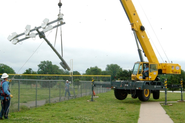 Workers with Tinker Support Services help Lynn Chapman, operator of a crane capable of lifting objects that weigh up to 30 tons, move a 65-foot light pole that was laying in the outfield of Tinker softball field #2. (Air Force photo by Mike Ray)