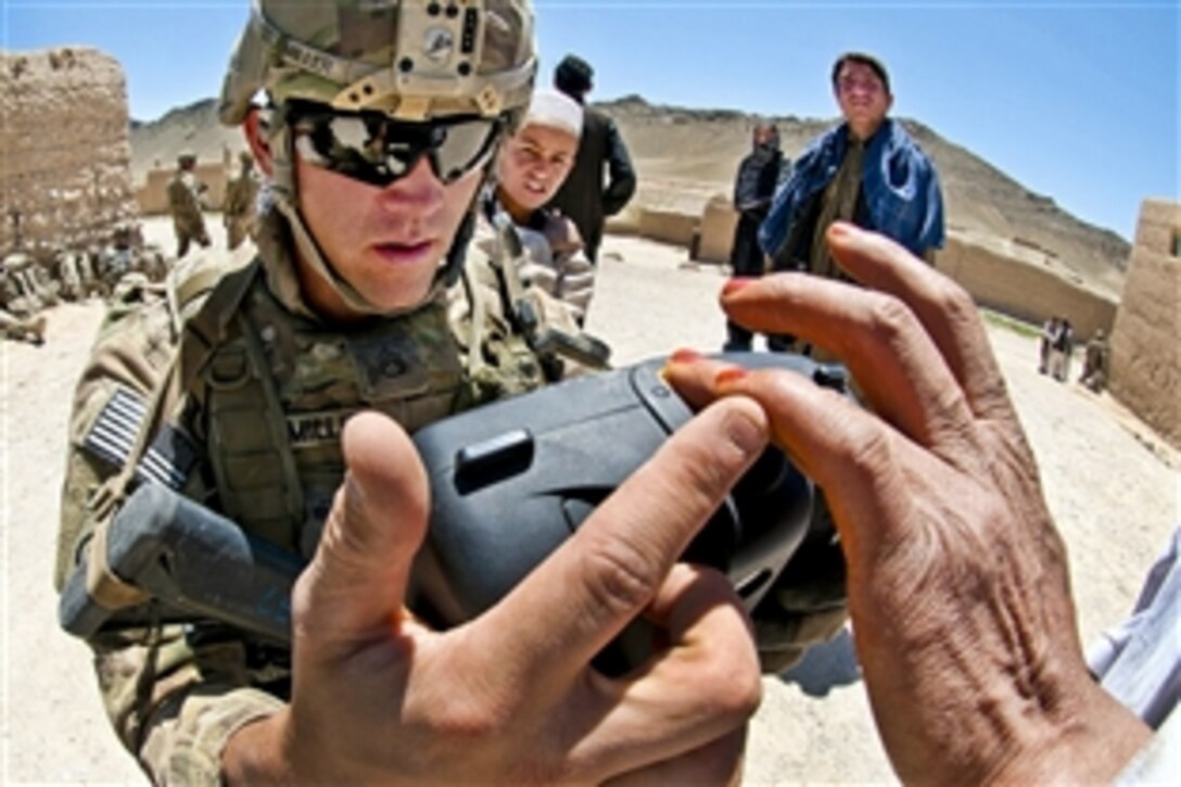 U.S. Army Staff Sgt. Mick Miller shows an Afghan villager how to place his finger on a handheld identity detection device to scan his fingerprint in Afghanistan's southern Ghazni province, May 4, 2012. Miller, a squad leader, is assigned to the 82nd Airborne Division’s 1st Brigade Combat Team.