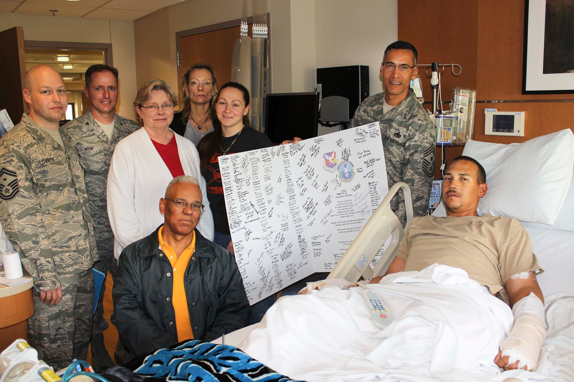 Supporters display an oversized get-well card as they gather around Staff Sgt. Brian Williams May 3 at the Walter Reed National Military Medical Center, Md. The card bears hundreds of signatures and well-wishes from Williams' home station family at Joint Base McGuire-Dix-Lakehurst, N.J. Williams, a military working dog handler from JB MDL's 87th Security Forces
Squadron, was deployed to Afghanistan where he was the victim of an improvised explosive device attack April 25. Williams suffered serious injuries when the IED detonated while he was on a mission outside Kandahar Airfield in southern Afghanistan. Visitors include: (from left) Senior Master Sgt. Vincent Lommen, 87th SFS first sergeant; Col. John Wood, JB MDL
and 87th Air Base Wing commander; Marge Williams, stepmother; Lionel Williams, father; Catherine Williams, mother; Staff Sgt. Emily Christofaro, 87th SFS; and Chief Master Sgt. Terrence Greene, 87th ABW and JB MDL command chief. Williams hails from Phoenix, Ariz. (U.S. Air Force courtesy photo/Released)

