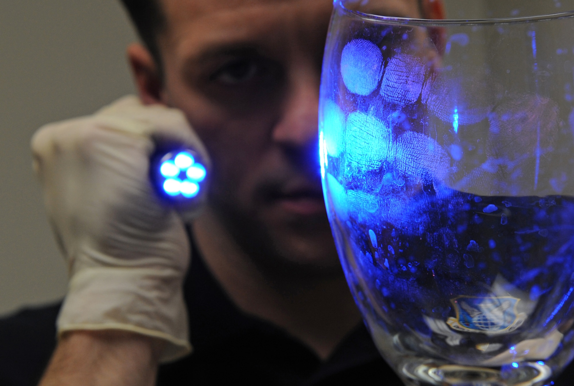 Special Agent Adam Deem, Air Force Office of Special Investigation Detachment 219, shines light on a glass to reveal fingerprints on Barksdale Air Force Base, La. Deem dusted the glass with an orange powder that helps agents detect finger prints with ultraviolet light.(U.S. Air Force photo by Airman 1st Class Micaiah Anthony)