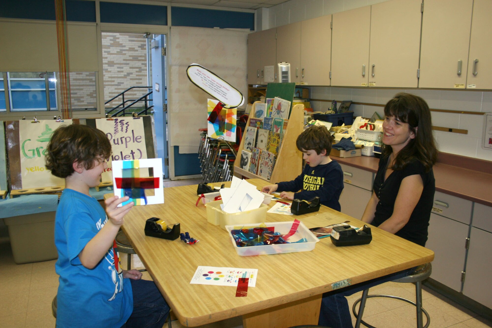 HANSCOM AIR FORCE BASE, Mass. – Mollie Gorman looks over projects that her sons Daniel (center) and Ryan (left) work on during Curriculum Night May 2 at the Hanscom Primary School. As part of the night’s activities, students and their families were invited to visit all of the classrooms and teachers and do a variety of activities together, including writing stories, making science projects and displaying new skills learned during wellness classes. (Courtesy photo)
