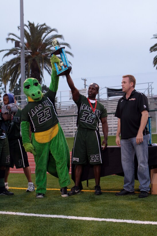 The Assault Amphibious School Battalion Gators mascot and Brian Richardson hold up the second place trophy given to them during the 2012 Flag Football Championship League on Camp Pendleton, May 17. Every player on both teams recieved medals for making it to the finals. Richardson is the offensive coach for the Gators.