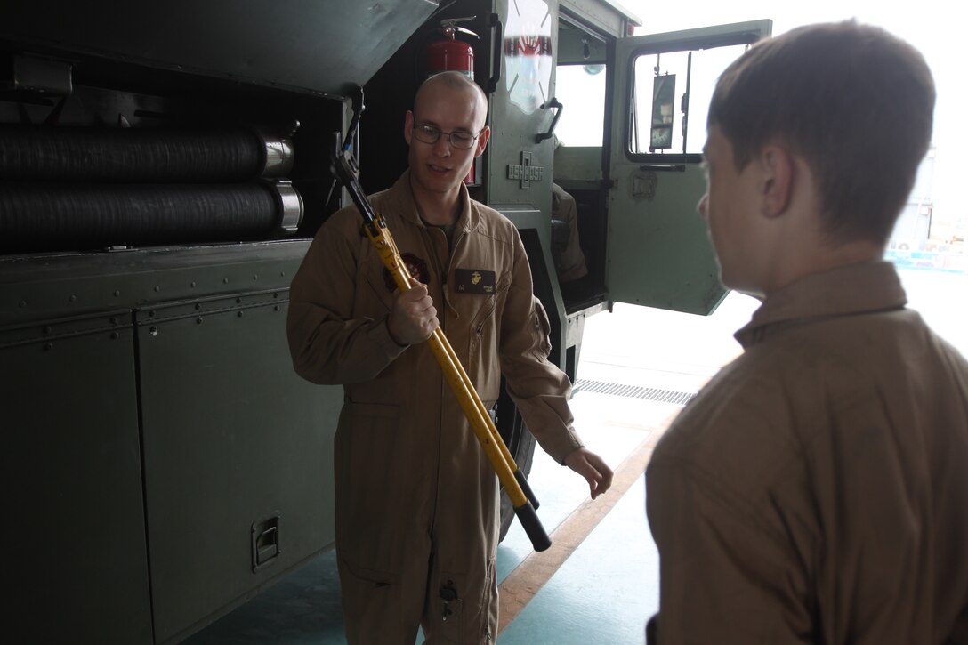Cpl. John T. Ritchie, station Aircraft Rescue Firefighter, shows a bolt cutter, which is stored in one of the many compartments aboard a P-19 fire truck, to Matthew C. Perry High School students during a job shadow day at the ARFF firehouse here May 17, 2012. The students spent the day following ARFF Marines as they went about their daily routine.