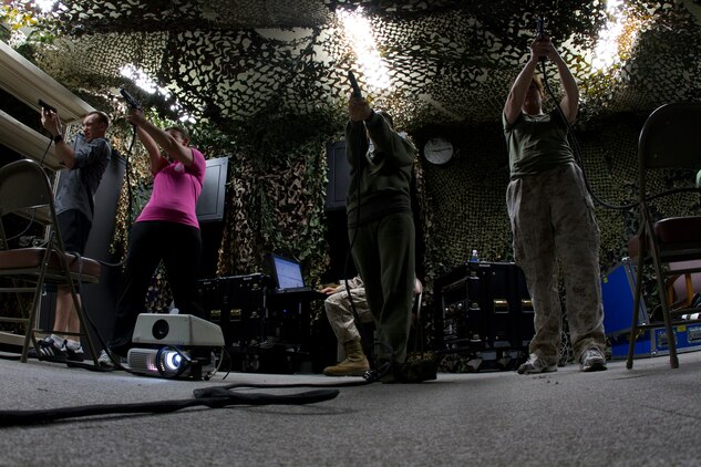 Marine spouses fire simulated rounds at the indoor simulated marksmanship trainer during Jane Wayne Day aboard Marine Corps Air Station Iwakuni, Japan, May 19. Jane Wayne Day lets family members experience parts of Marine Corps life to provide shared experience and understanding.