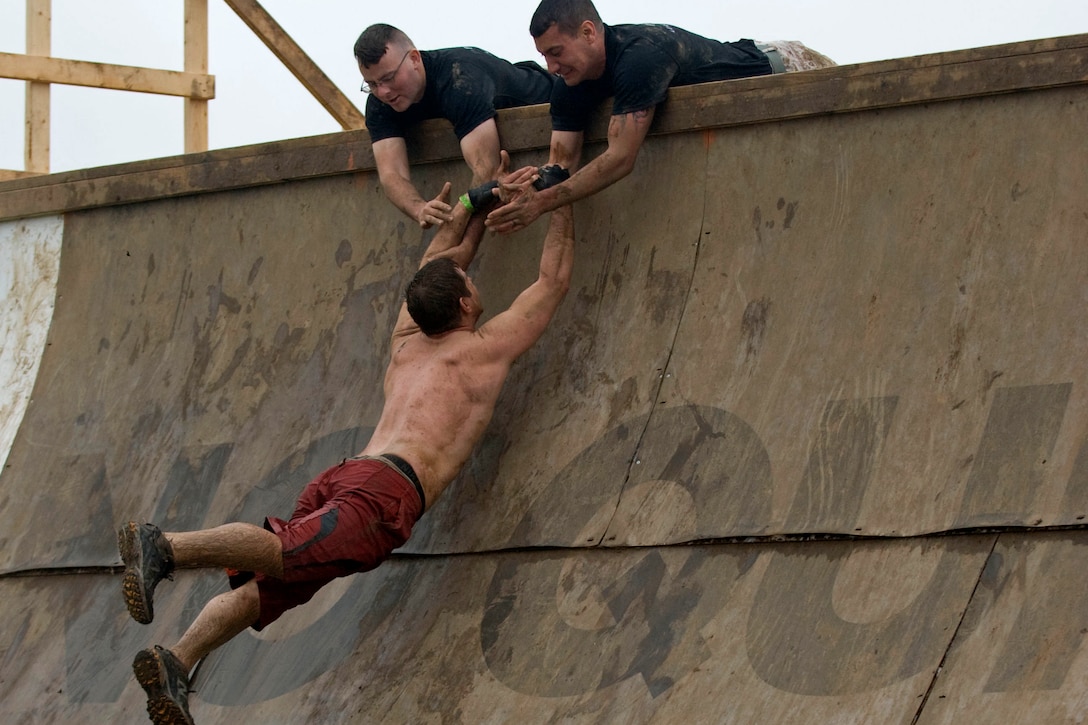 Volunteers Staff Sgt. Clinton F. Firstbrook and Sgt. Nicholas J. Bynum, both with Recruiting Station Twin Cities, help competitors up an obstacle named Everest during Tough Mudder Twin Cities May 20. Everest is a quarter pipe that is designed with teamwork in mind. Few can scale this obstacle without help from their fellow participants.