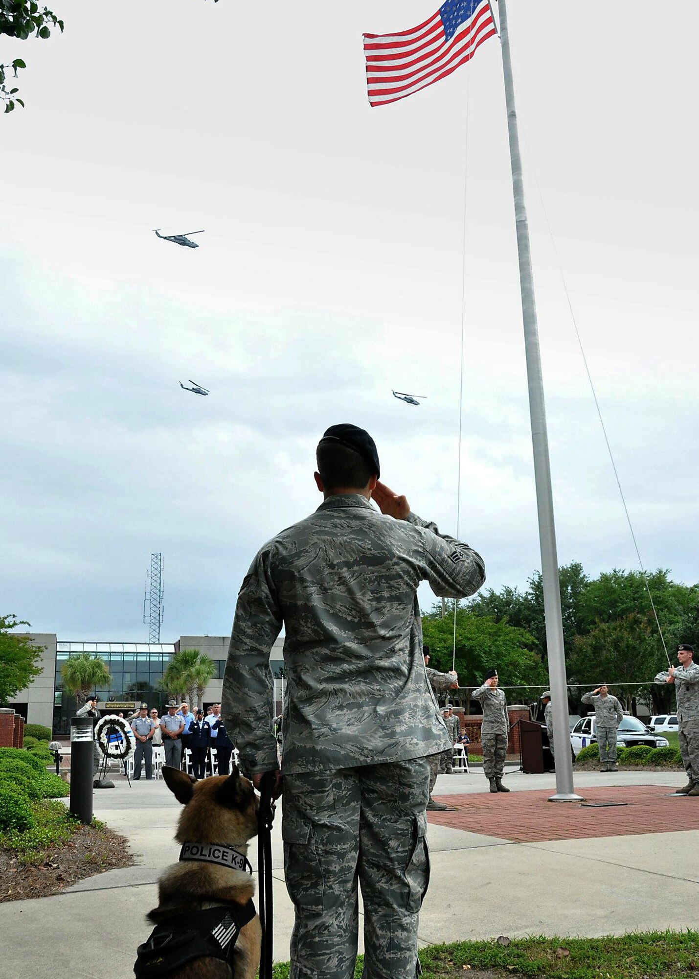 A 628th Security Forces Squadron dog handler and his military working dog Elmo show respects to the flag as it is lowered while a trio of Cobra helicopters flies over during the Joint Base Charleston 2012 National Police Week memorial retreat ceremony at the base flagpole May 18, 2012.  (U.S. Air Force photo / Michael Dukes)