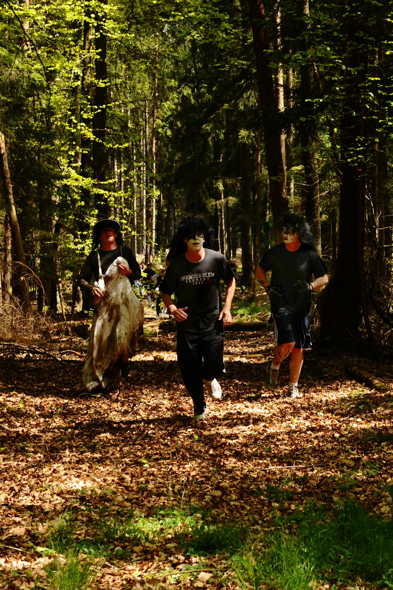 SPANGDAHLEM AIR BASE, Germany – Members from team Kiss and a Groupie run through the forest during the Tier II Mud-Run outside of base here May 17. The mud-run consisted of 17 teams, which ran five kilometers through various obstacles and competed for best costumes. The event raised more than $2,000 for the Wounded Warrior Project in Landstuhl. (U.S. Air Force photo by Airman 1st Class Dillon Davis/Released)