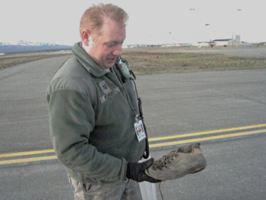 JOINT BASE ELMENDORF-RICHARDSON, Alaska -- Tech. Sgt. Scott Hopkins, an electrical enviroonmental specialist from the 176 Maintenance Squadron, checks out an old shoe found by a co-worker May 14 during the annual Foreign Object Airfield Clean-up Walk. Military members across the base joined efforts  to clean up the airfield here after the snow melted this Spring. The members collected over 1,970 pounds of foreign objects.