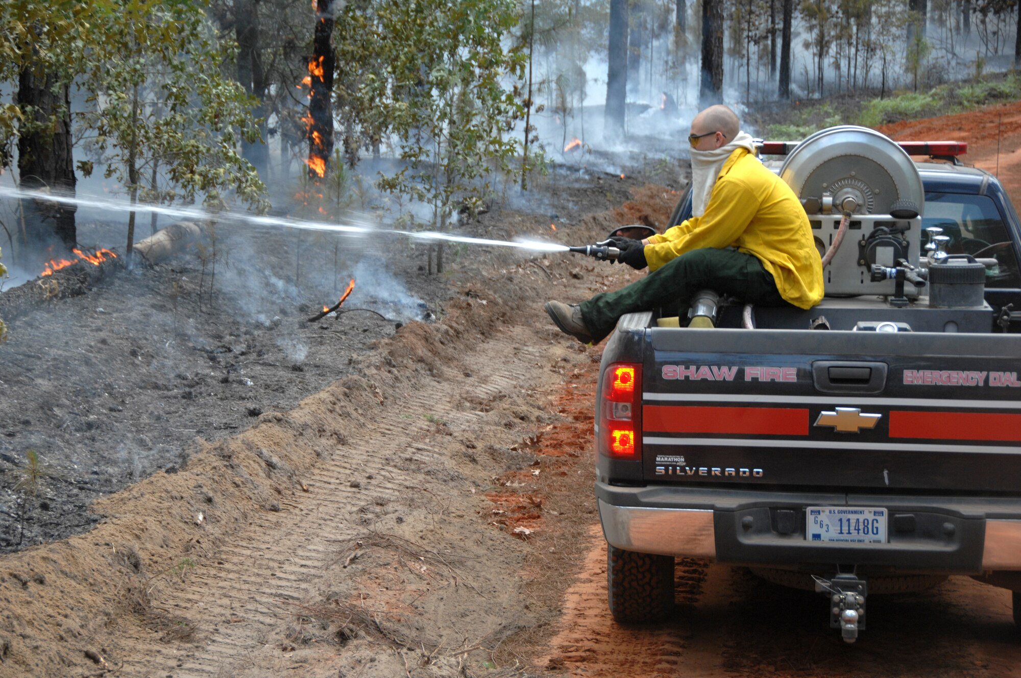 U.S. Air Force Airman Clayton Angeloff, 20th Civil Engineer Squadron firefighter, hoses down trees and shrubs to reduce the potential damage of a fire at Poinsett Electronic Combat Range, S.C., May 21, 2012. Shaw’s firefighters responded quickly to a 150-acre blaze at the Poinsett Range training site. (U.S. Air Force photo by Airman 1st Class Blake Hubbard/Released)