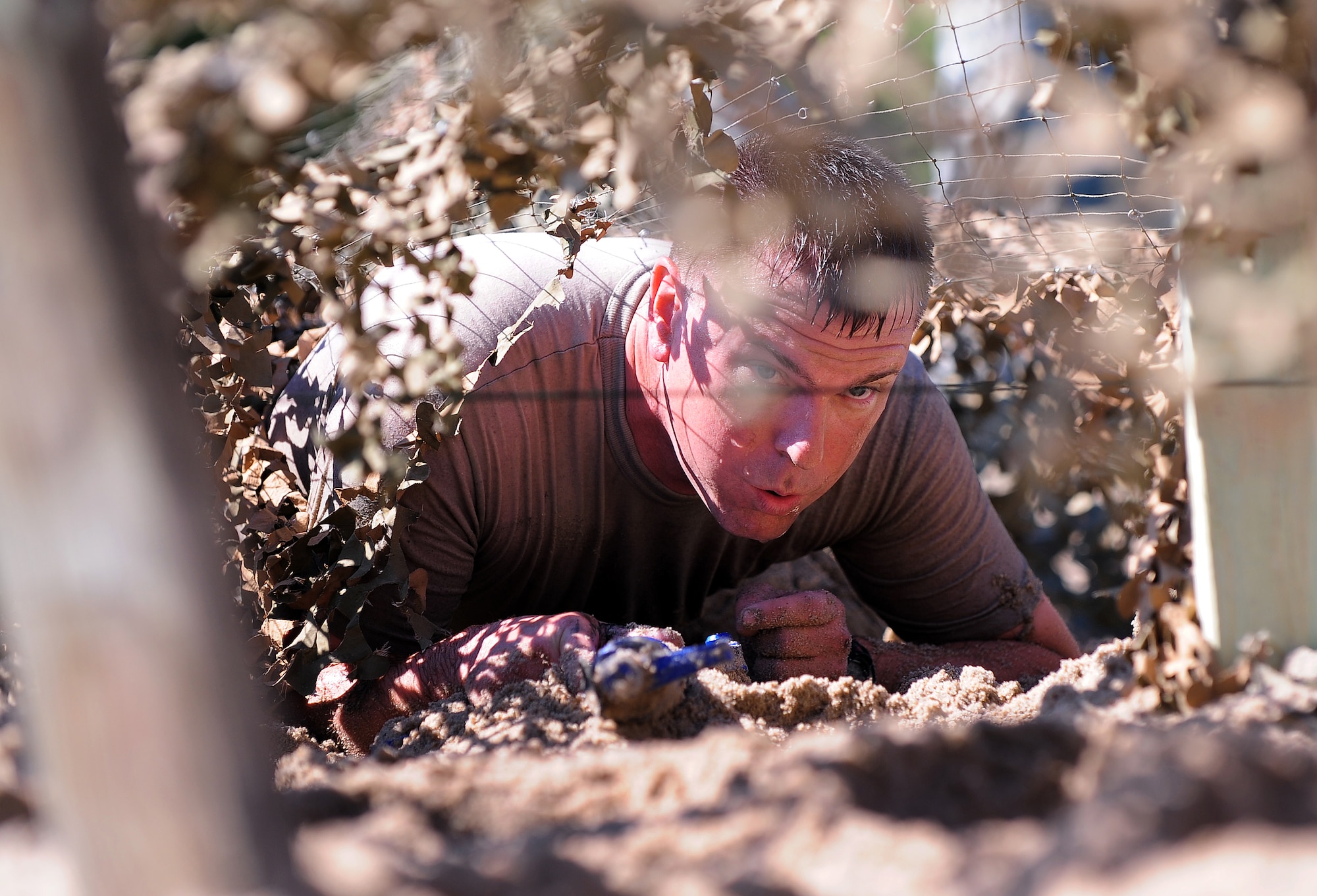 U.S. Air Force Master Sgt.  Chad Frahm, 55th Security Forces Squadron, crawls through sand under a camouflage canopy sitting just inches from the ground as he makes his way through one of the obstacles set up for the "Evasion Challenge" put on by 55th SFS as part of National Police Week May 16 at Offutt Air Force Base, Neb.  During National Police Week there was also a weapons display, golf tournament and a retreat ceremony.  (U.S. Air Force photo by Josh Plueger)