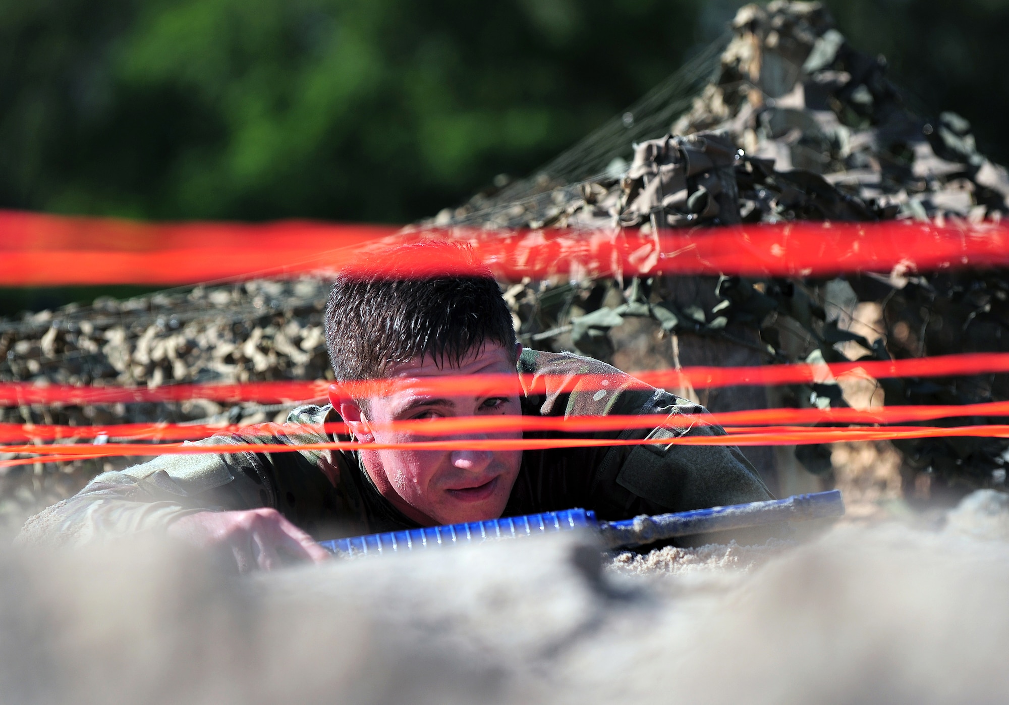 U.S. Air Force Airman First Class Kenneth Jenkins, 55th Security Forces Squadron, crawls through loose sand and under red cables just inches above him as he makes his way through an "Evasion Challenge" put on by 55th SFS as part of National Police Week May 16 at Offutt Air Force Base, Neb. Jenkins and his team faced several obstacles in the challenge testing participants both physically and mentally.  (U.S. Air Force photo by Josh Plueger)