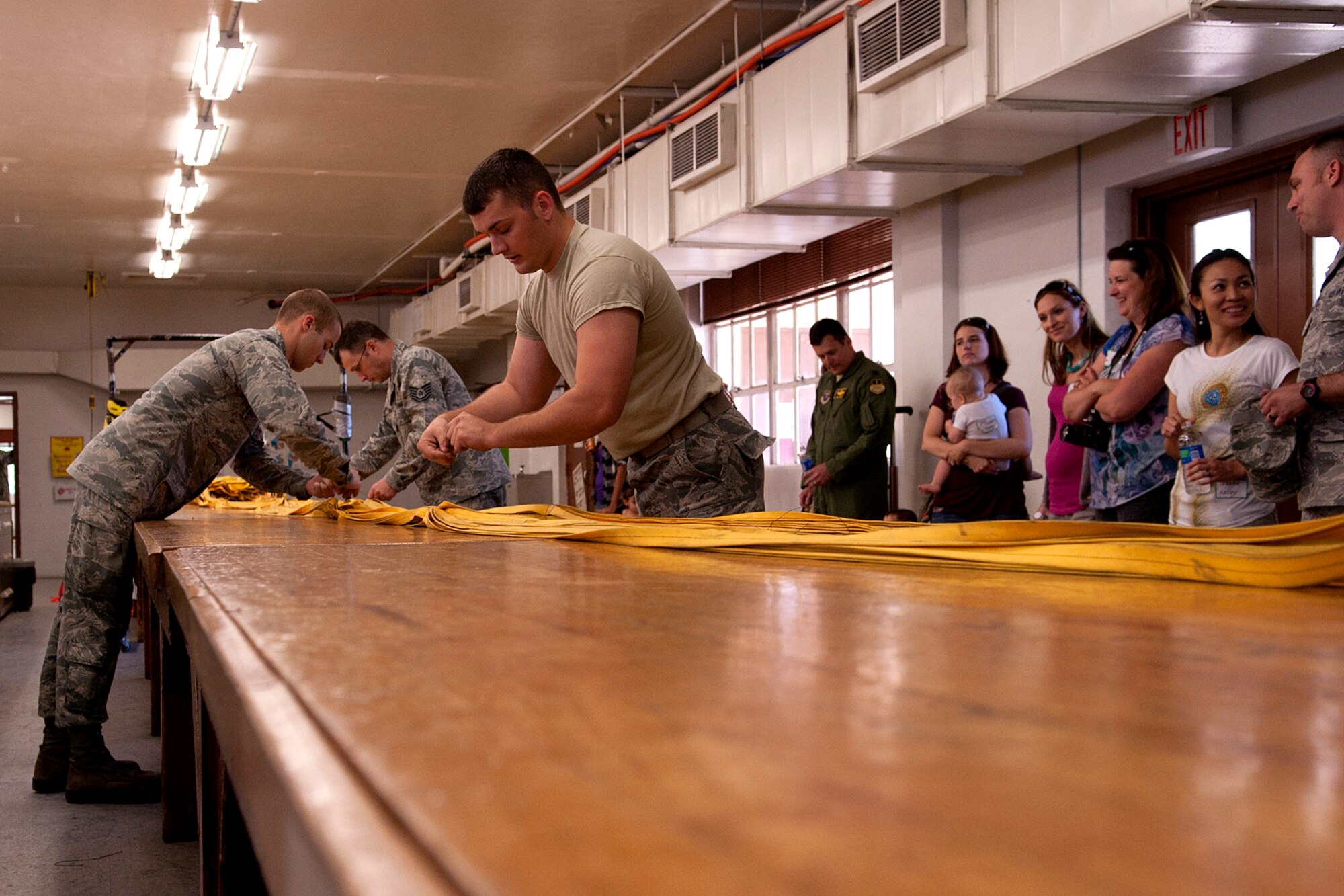 U.S. Air Force Airman First Class Richard James and Jacob Rash, 2nd Operations Support Squadron (OSS) Aircrew Flight Equipment (AFE) technicians, assist Technical Sgt. Wesley Vinson, 2nd OSS Parachute Shop noncommissioned officer in charge, with repacking a B-52H Stratofortress drag chute during Spouse Appreciation Day, May 22, 2012. Spouses of members of the 2nd OSS were treated to a tour of the AFE shop and even participated in a chute repacking. (U.S. Air Force photo by Master Sgt. Greg Steele/Released)