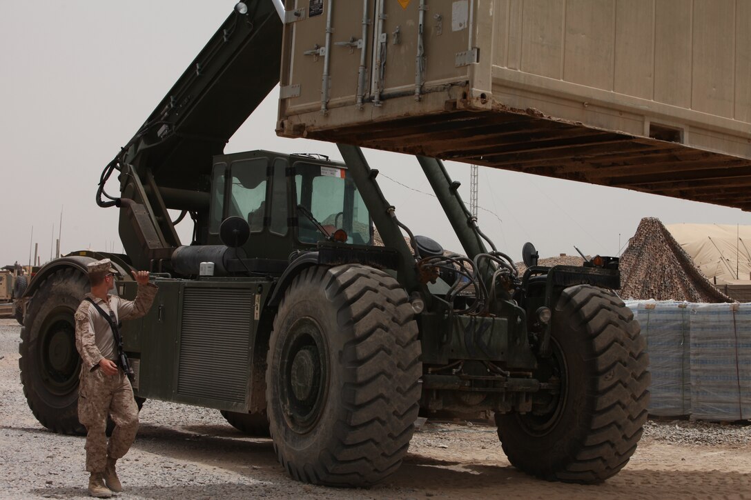 Cpl. Malcolm Smith, embarkation and logistics specialist, Headquarters and Support Company, 2nd Battalion, 9th Marines, Regimental Combat Team 5, ground guides a heavy equipment operator using a Kalmar Rough Terrain Container Handler at Forward Operating Base Hanson, May 25. The Kalmar is one of the only heavy equipment vehicles that can lift ISOs, which are 20-foot containers the Marine Corps uses to store gear and equipment.