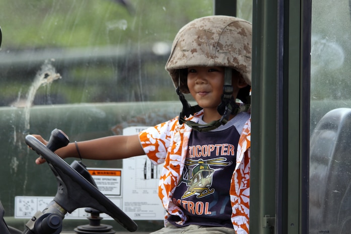 A child tries on and plays with gear from a Marine Wing Support Squadron 171, Marine Aircraft Group 12 static display while attending a historic Memorial Day service on North Field on the island of Tinian May 28, as servicemembers take a reprieve from participating in Exercise Geiger Fury 2012.