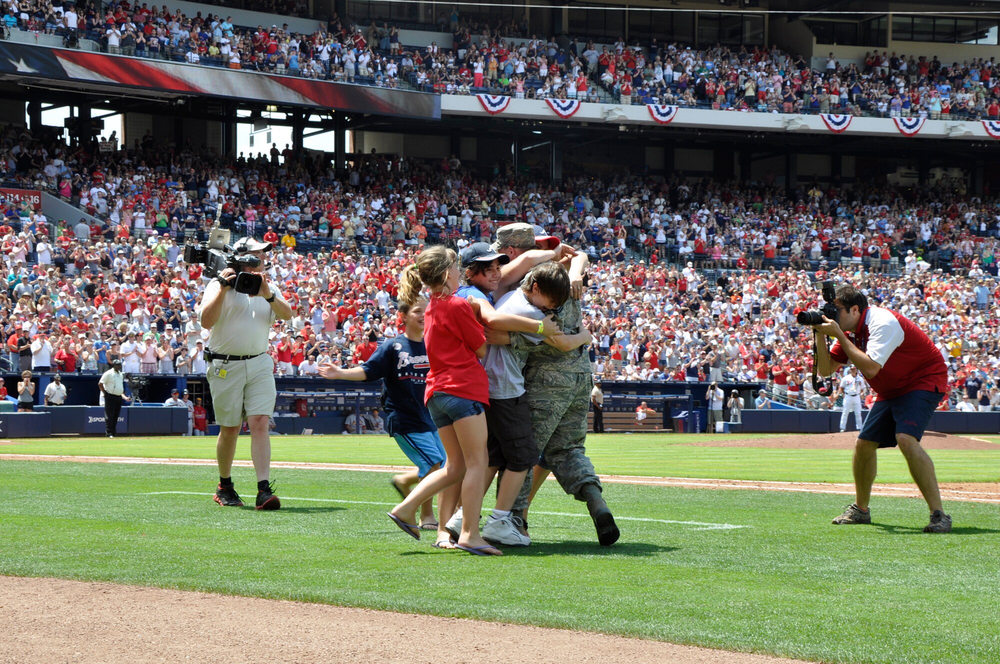 Master Sgt. David Sims and his family embrace during a surprise homecoming May 28 at the Braves baseball game at Turner Field in Atlanta. Sims was returning from a six-month deployment from Kabul, Afghanistan. His family was attending the Braves game and were called onto the field at the top of the fifth inning for a special video tribute from Sims, who they thought was still in Afghanistan. At the end of the video, Sims told them to “wait a minute.” Then, from the other side of the Braves dugout, he appeared and the family raced across the baseball field for the heart-warming reunion witnessed by thousands of applauding fans. Sims is assigned to Headquarters Air Force Reserve Command’s Communications Directorate at Robins Air Force Base, Ga. (Defense photo/Jessica Blanton)