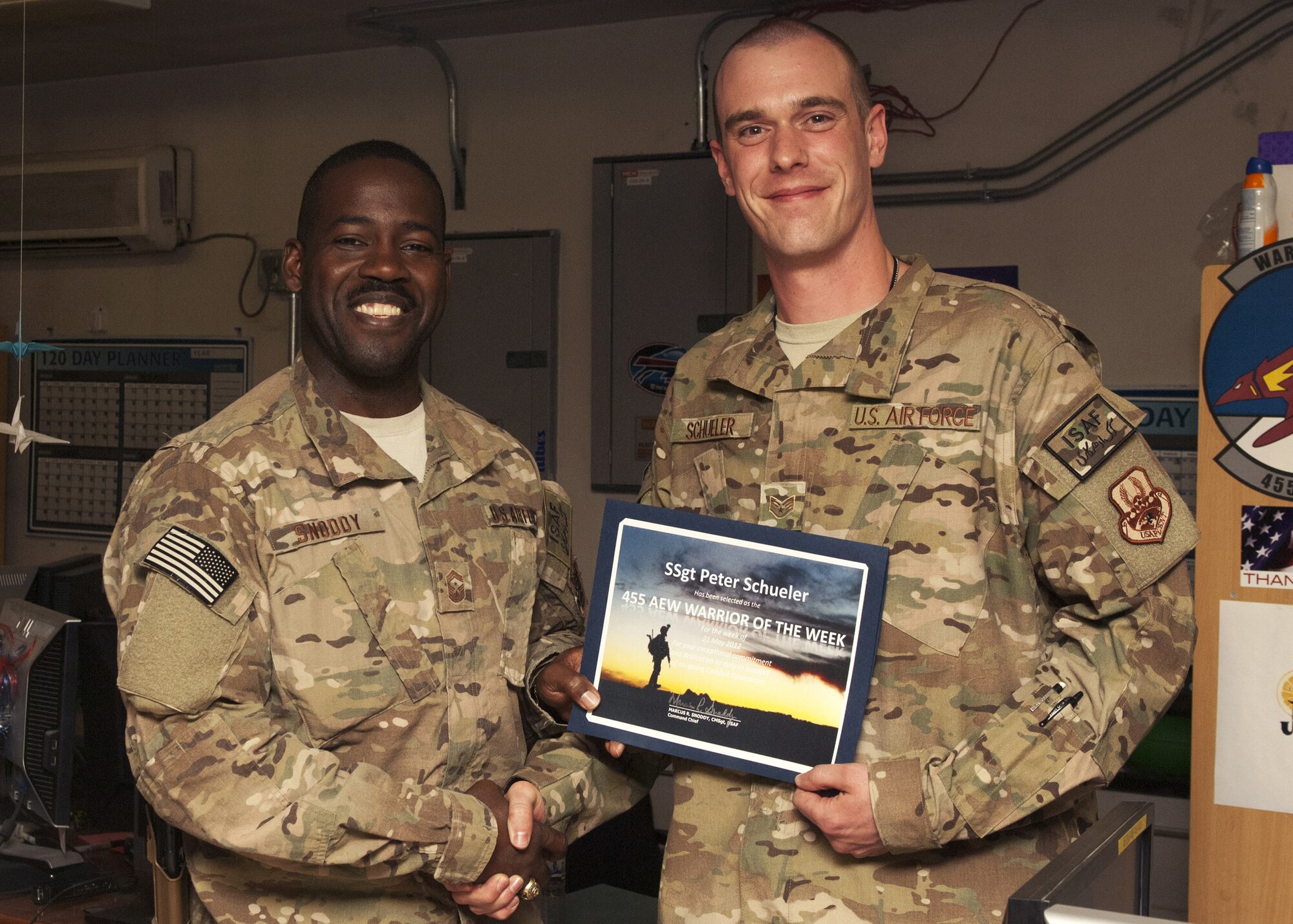 Chief Master Sgt. Marcus Snoddy, 455th Air Expeditionary Wing command chief, presents the Warrior of the Week award to Staff Sgt. Peter Schueler, 455th Expeditionary Operations Support Squadron, noncommissioned officer in charge of Current Ops, at Bagram Airfield, Afghanistan, 29 May, 2012. Schueler co-created the new metric slides and the Situation Report database for the 455th Expeditionary Operations Group, allowing the critical metrics of eight squadrons to become automated across Bagram. (U.S. Air Force photo/Staff Sgt. Jeff Nevison)