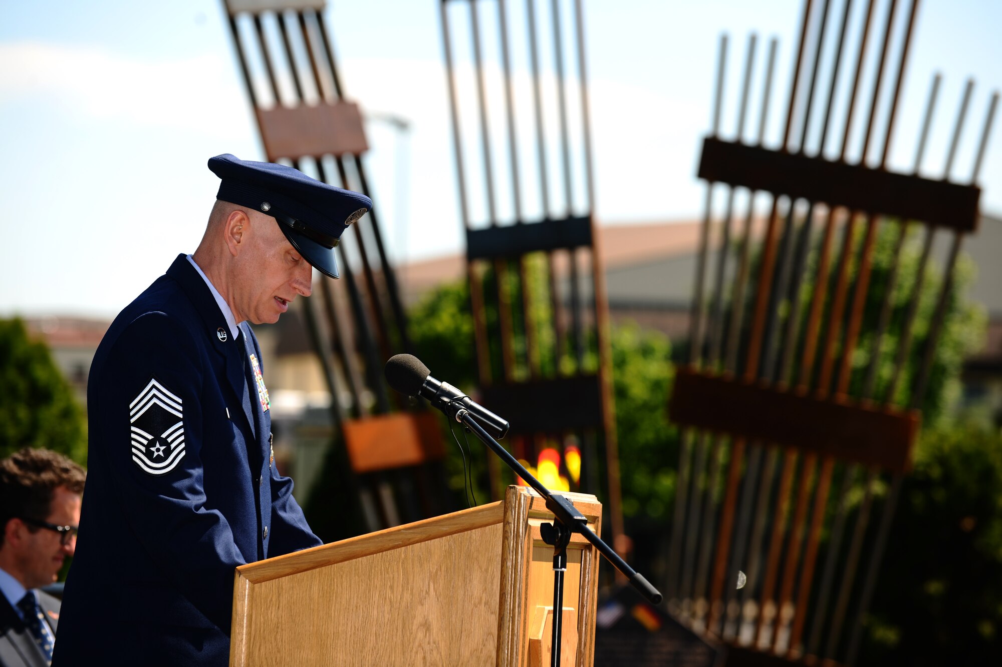 SPANGDAHLEM AIR BASE, Germany – Chief Master Sgt. Richard Lien, 52nd Civil Engineer Squadron fire chief, speaks during the 9/11 memorial dedication and wreath-laying ceremony here May 25. The 9/11 memorial was donated to the 52nd Fighter Wing by the Host Nation Council Spangdahlem and local businesses.  The sculpture was designed by Hubert Kruft, artist, from Niederpruem. (U.S. Air Force photo by Airman 1st Class Matthew B. Fredericks/Released)
